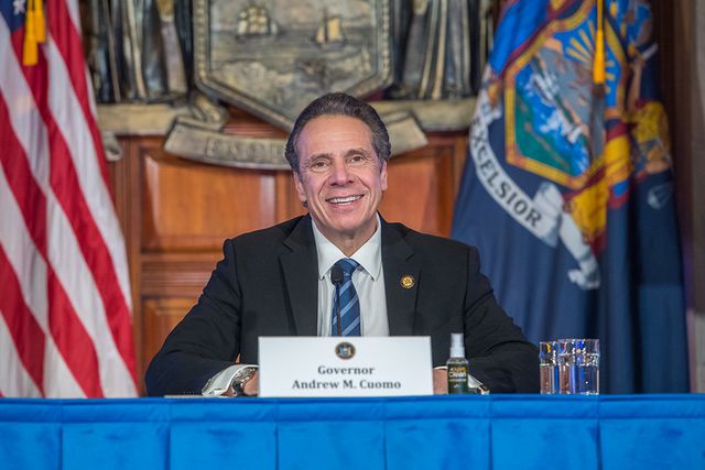 Governor Andrew Cuomo sits at a table and smiles during a press briefing on Wednesday, January 6, 2021.